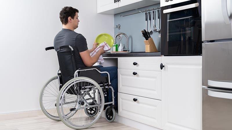 Man in wheelchair at kitchen sink.