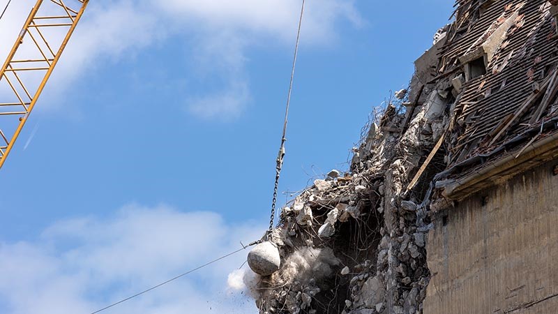 Heavy wrecking ball crane demolishing old building.
