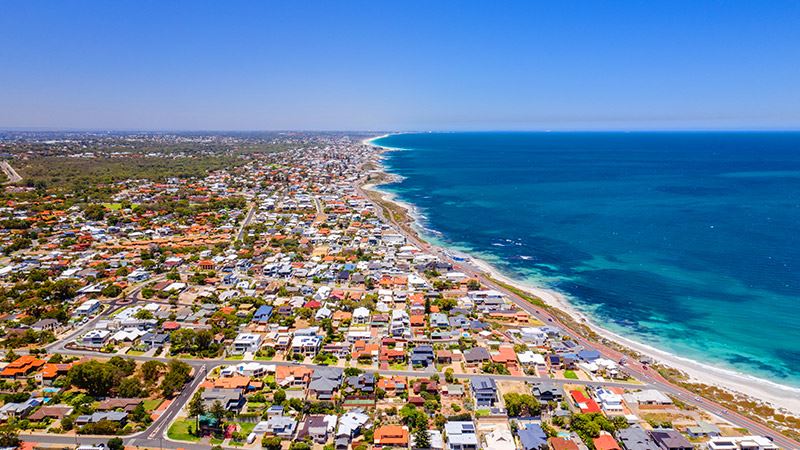 Aerial drone shot of the Hillarys and Sorrento coastline, looking towards Perth city centre at mid day. Bright blue ocean water and beach surround the suburbs.