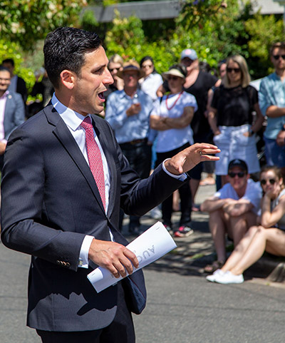 Auctioneer in suit address kerbside crowd of potential buyers