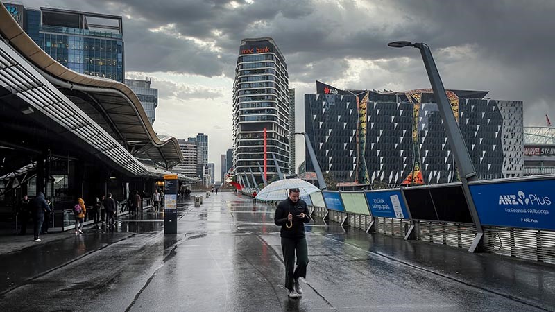 Pedestrians walking along Southern Cross Bridge in Melbourne, among tall modern commercial buildings.