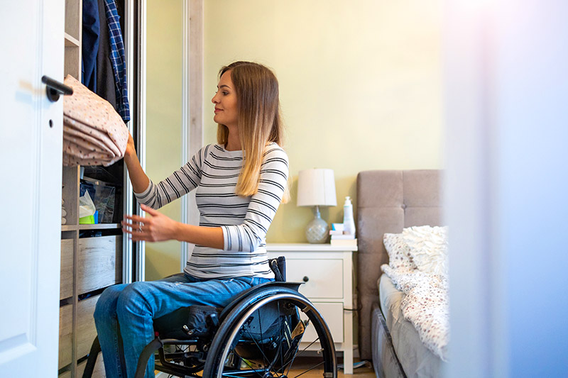 Woman in wheelchair retrieving item from bedroom shelf